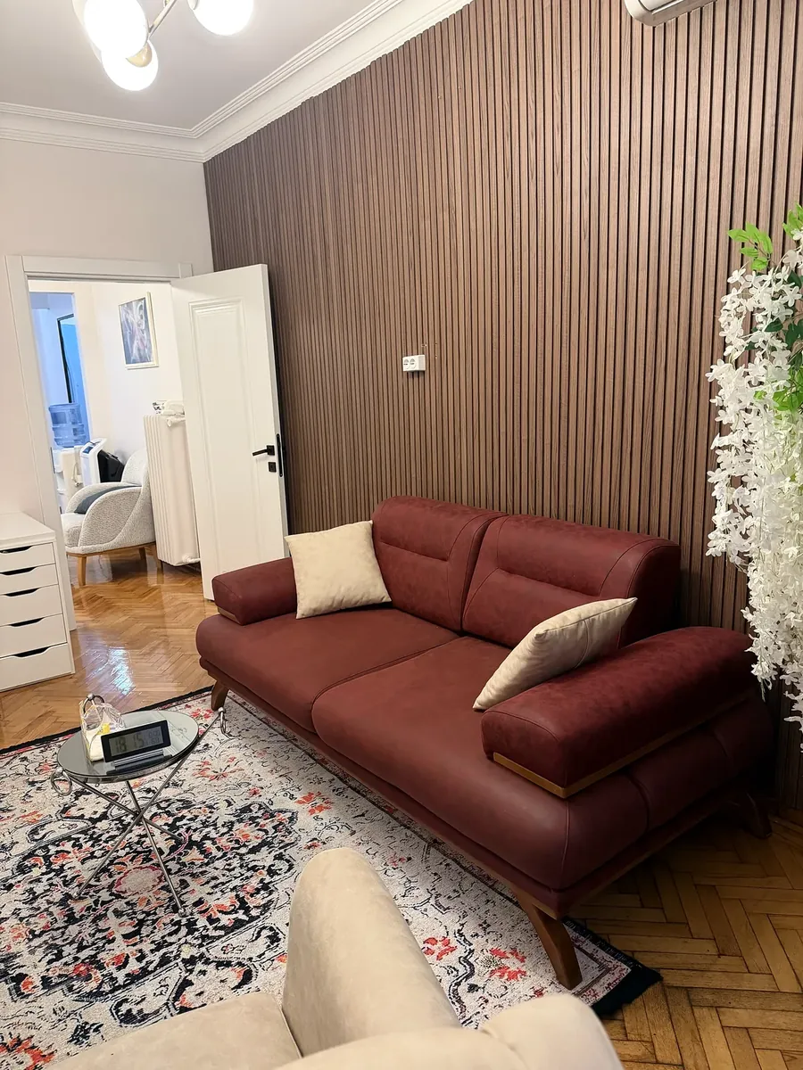 Ahşap çıtalı duvar ve bordo kanepe, arkada açık kapı