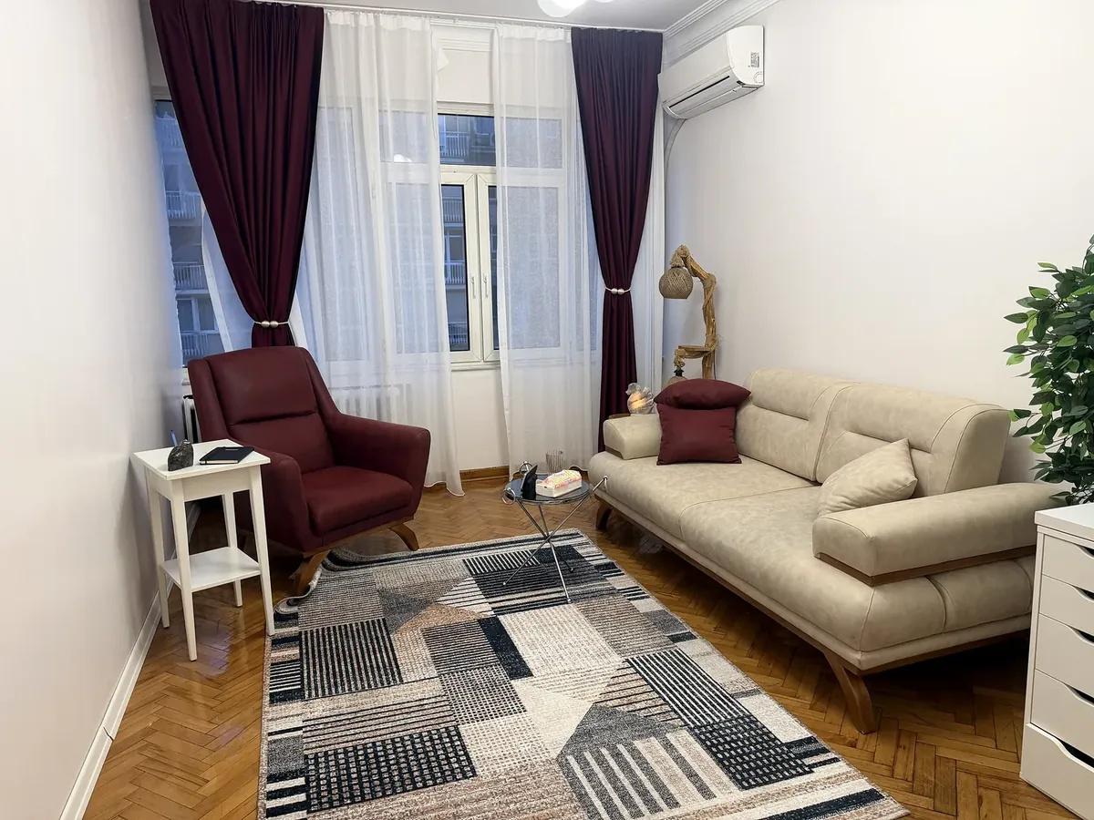 Bordo berjer, krem kanepe ve geometrik desenli halısıyla ofis